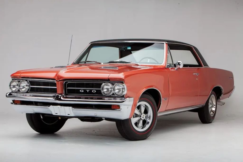 1964 Pontiac GTO in red with chrome bumper, split grille and Pontiac arrow emblem, three-quarter front view.