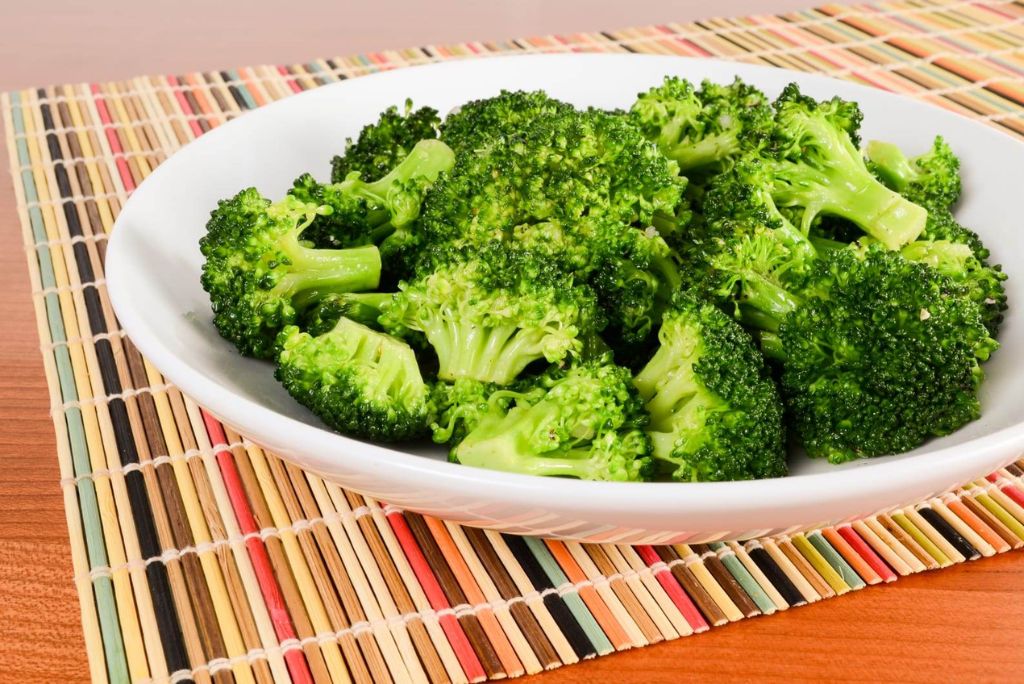 A bowl of fresh, steamed broccoli served on a colorful woven placemat.