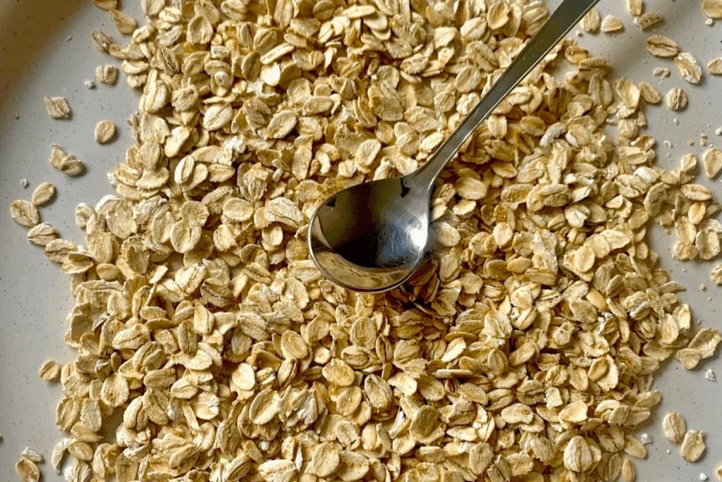 A close-up of rolled oats scattered on a plate with a spoon resting on top.