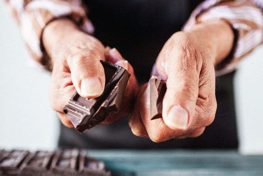 A person breaking a piece of dark chocolate with their hands.