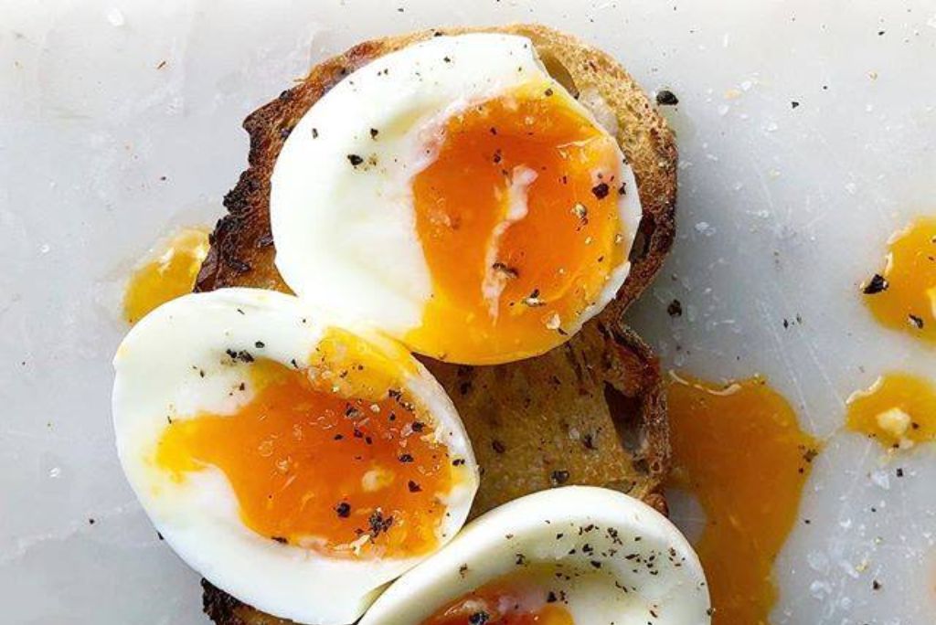Three soft-boiled eggs with runny yolks served on toasted bread, sprinkled with black pepper and sea salt.